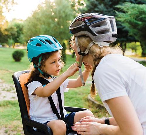 一个孩子坐在自行车的后座上，帮助他的母亲系上头盔